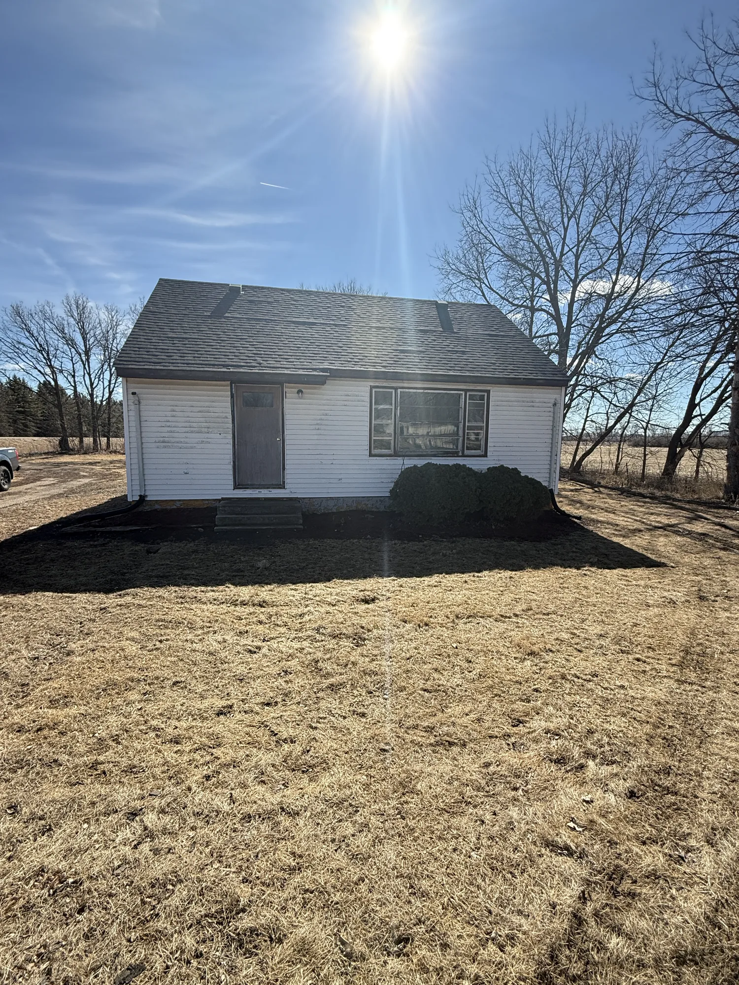 The Austin farmhouse before restoration in winter, with worn siding, an aging roof, bare trees, and dead grass