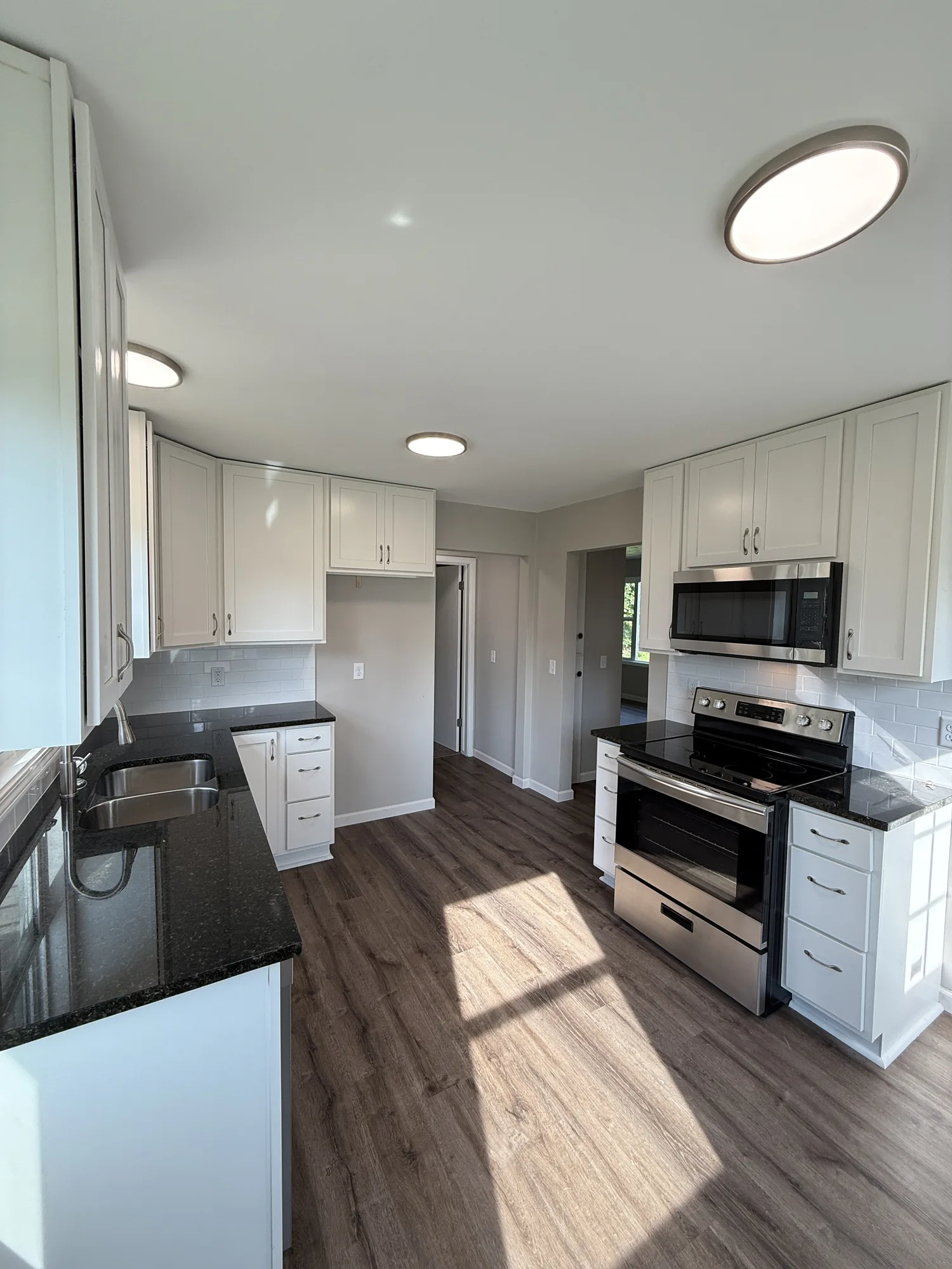 Fully restored kitchen with new white shaker cabinets, dark countertops, stainless appliances, subway tile backsplash, and new flooring