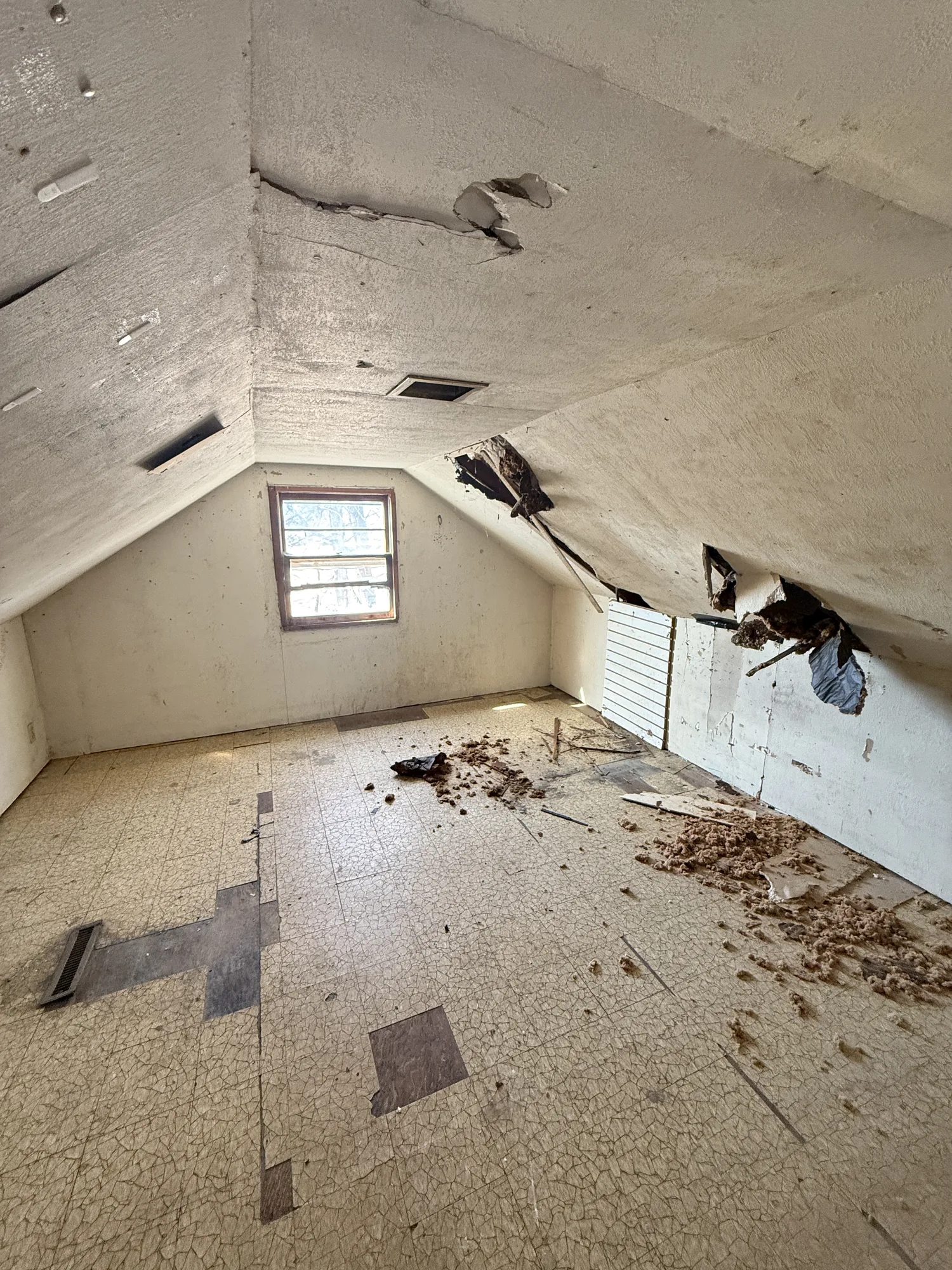 Water-damaged attic with holes in the ceiling, exposed structure, and debris over cracked tile flooring