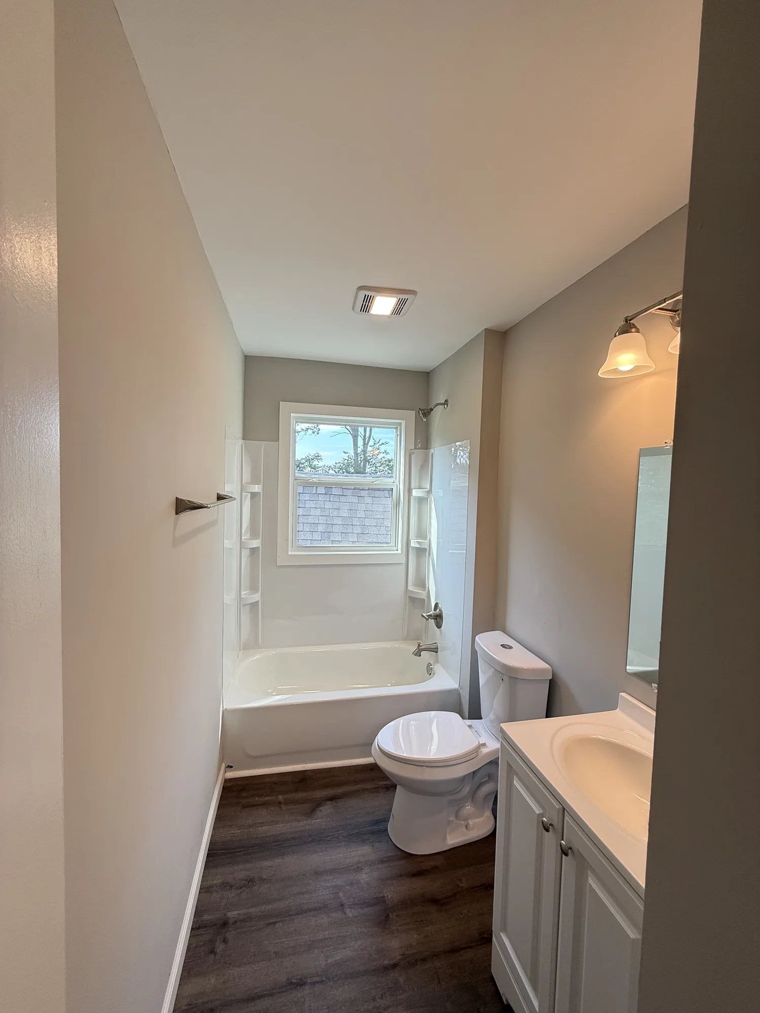 Finished bathroom with new tub and shower surround, vanity, fixtures, flooring, and fresh neutral paint
