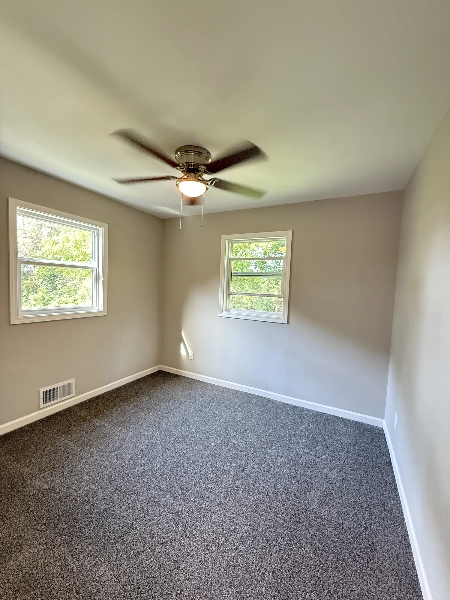 Finished bedroom with new gray carpet, repaired ceiling with a ceiling fan, new windows, and fresh neutral paint