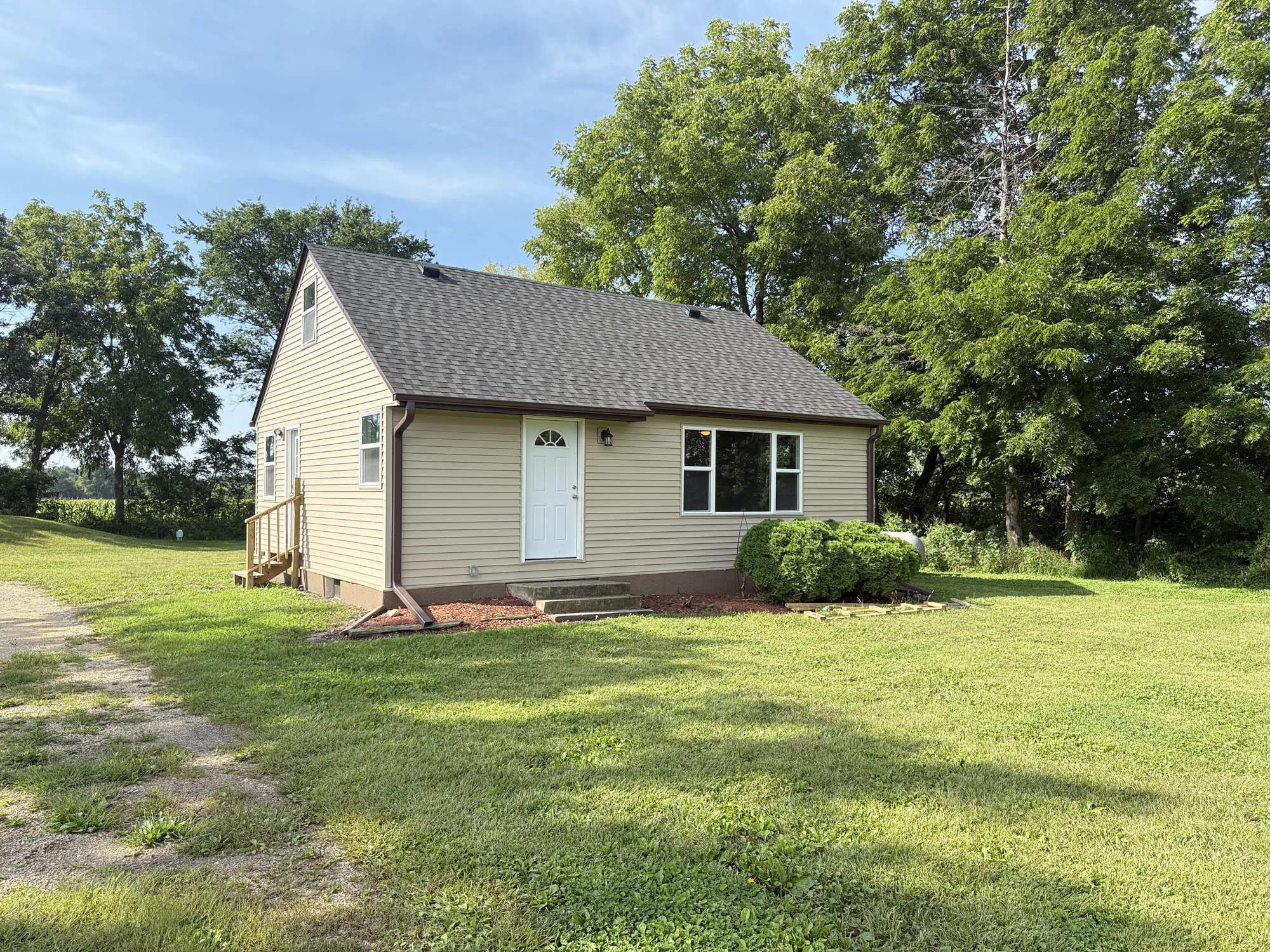 The finished farmhouse in summer with new siding, a new roof, new windows and entry door, and a green lawn