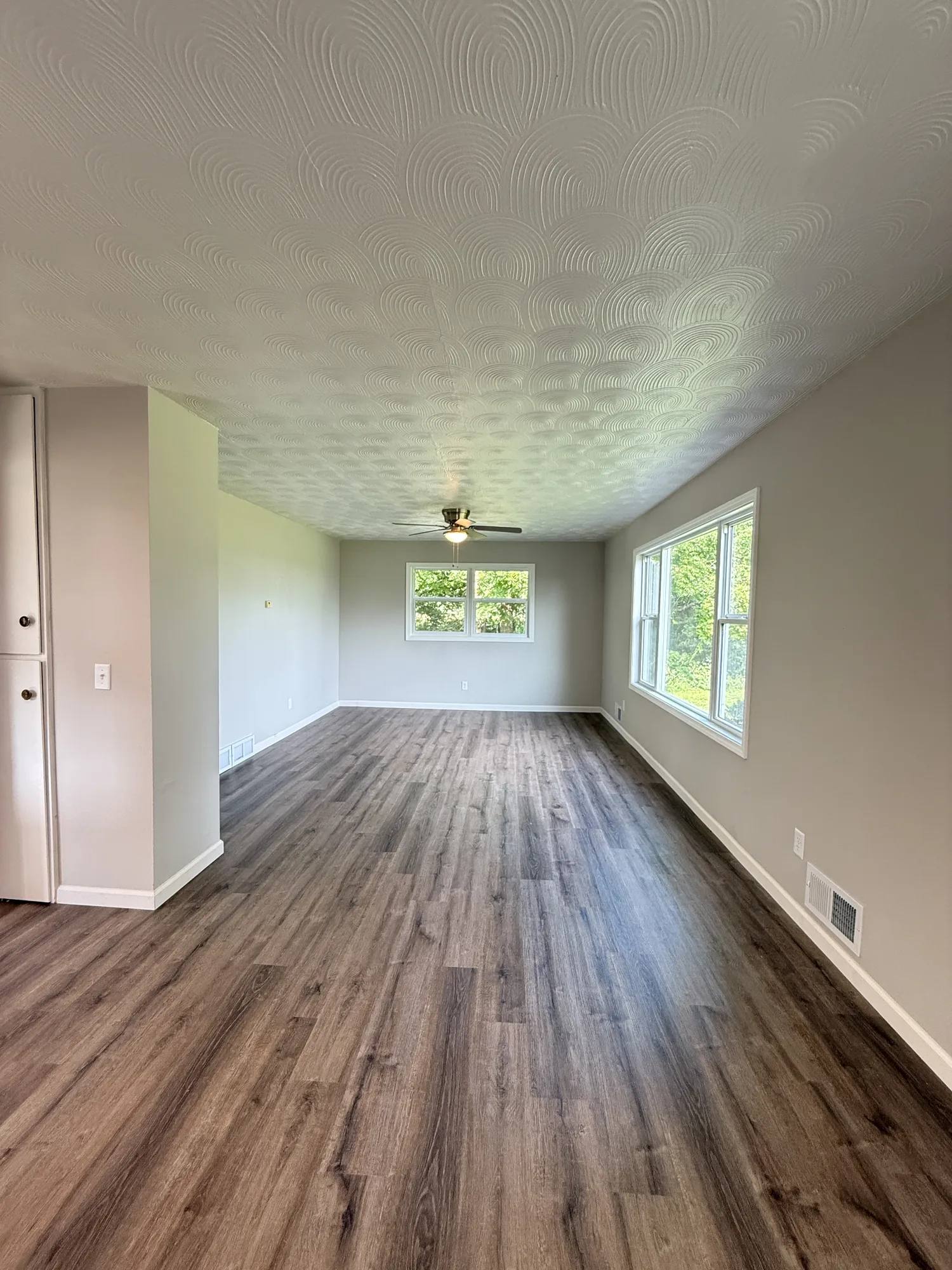 Restored living room with new wood-look flooring, fresh paint, new trim and windows, and a refinished textured ceiling with ceiling fan